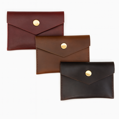 Three leather card holders in brown, brown with gold button, and black with gold button on a white background.